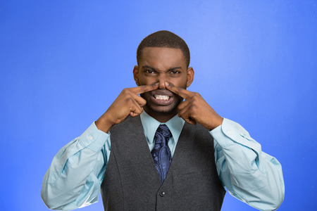 Closeup portrait young executive man, disgust on face, pinches his nose, something stinks, bad smell, situation isolated blue background. Negative emotion facial expression, perception body languageの写真素材