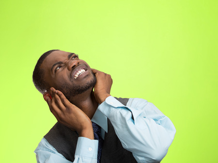 Closeup portrait young angry mad unhappy stressed man covering his ears looking up, to say stop making loud noise it's giving me headache isolated green background. Negative emotion, face expressionの写真素材