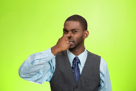 Closeup portrait young executive man, disgust on face, pinches his nose, something stinks, bad smell, situation isolated green background. Negative emotion facial expression, perception body languageの写真素材
