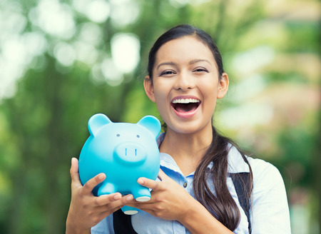 Closeup portrait happy, smiling business woman, bank employee holding piggy bank, isolated outdoors indian autumn background. Financial savings, banking concept. Positive emotions, face expressionsの写真素材