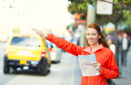 Girl calling taxi cab in New York City, holding city map standing on sunny summer day in street of Manhattan, USA. Beautiful young woman outdoor on her vacation trip. Positive face expression, emotionの写真素材