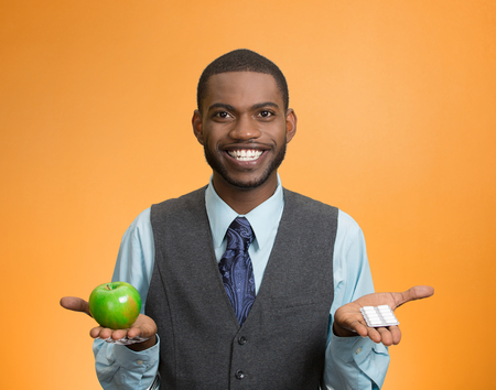 Portrait young, fit, happy executive man holding green fresh apple in one hand, pills, vitamins in another. Sugar free chewing gum, dentist recommended. Face expressions, emotion, health care. Dietingの写真素材