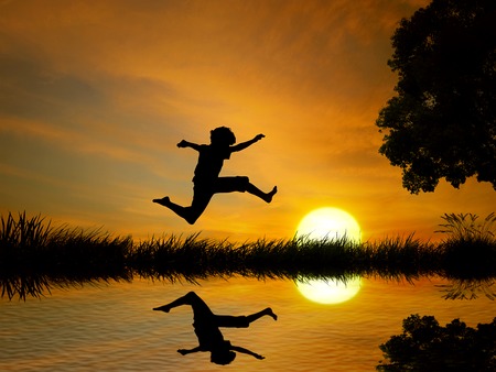 Happy boy, teenager jumping in water, over lake with sunset background, body reflection in water. の写真素材