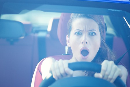 Dear in headlights. Fright face woman driving car, wide open mouth eyes, strongly squeezing wheel, front window view. Negative human face expressions, emotions, reaction. Road trip risk danger conceptの写真素材