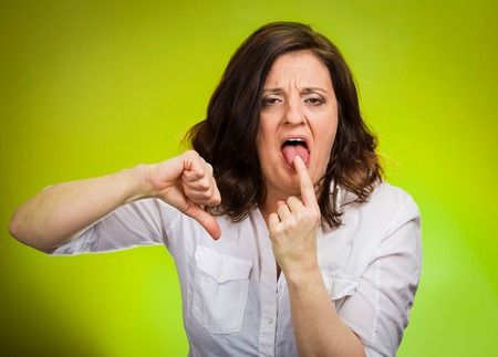 Disgust thumbs down gesture. Portrait unhappy angry pissed off woman finger in mouth gesture looking with negative facial expression disapproval isolated green background. Human emotion reactionの写真素材