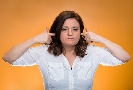 Closeup portrait, mature woman covering plugging ears annoyed by loud noise ignoring someone not wanting to hear their your side story isolated orange background. Negative human emotion, expressionの写真素材