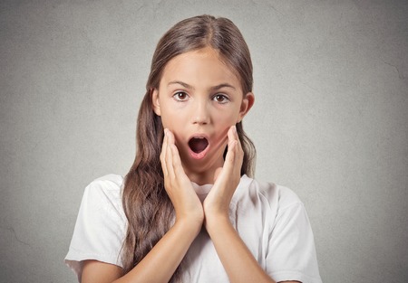 Surprise. Closeup portrait teenager girl shocked, wide open mouth eyes, jaw drop, blown away, isolated grey wall background. Human emotions, facial expression, feeling, body language, reactionの写真素材