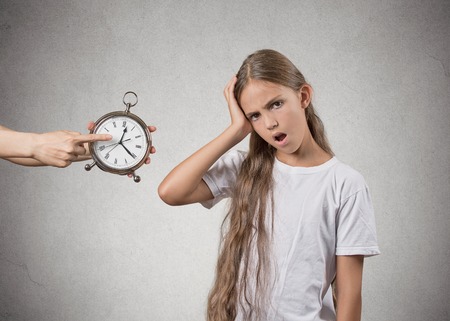 Time to go to bed. Portrait of mom showing kid clock that it is late. She doesn't like that, isolated grey wall background. Face expressions, emotions. Difficult parenting conceptの写真素材