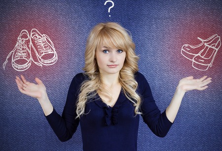 High heels or comfy sneakers that is a question. Confused woman deciding what should she wear to work, isolated blue background with shoes pictures. Female well being, comfort concept. Face expressionの写真素材