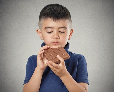 Kids love sweets. Portrait happy little boy eating whole bar of chocolate, isolated on grey wall background. Positive human emotions, face expressions. Food cravingsの写真素材