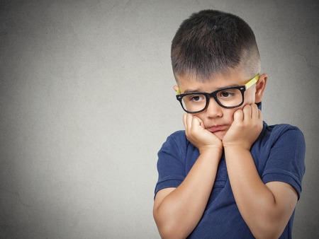 Sad, thinking. Closeup portrait headshot depressed, alone, tired child resting head on fist  isolated grey wall background. Negative human emotion face expression feeling life perception body languageの写真素材