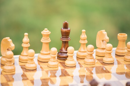 Closeup wooden chess figures with black king surrounded by white army on chessboard. Lost leader, politics, negotiation, strategy, power, tactic conceptの写真素材