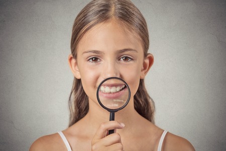 Headshot funny teenager girl showing teeth through a magnifying glass, isolated on grey wall background. Positive human face expressions, emotions. Children dental care conceptの写真素材
