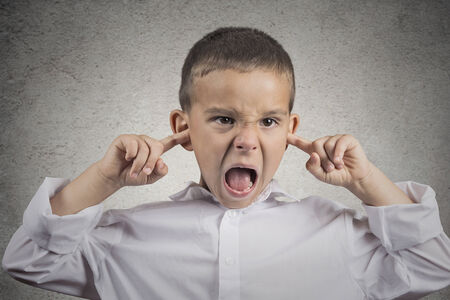 Closeup portrait angry annoyed pissed off boy plugs his ears with fingers sticking out tongue looking with funny negative facial expression, disapproval isolated grey wall background. Human emotionsの写真素材