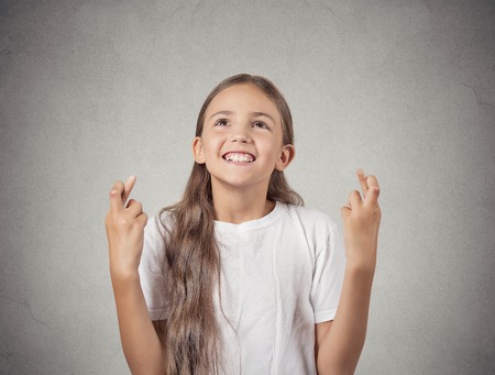 Closeup portrait excited smiling hopeful teenager girl crossing her fingers hoping, asking for best isolated grey wall background. Human face expression emotion feeling attitude reaction body languageの写真素材