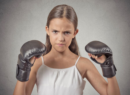 Aggressive child teenager girl wearing boxing gloves ready to fight isolated grey wall background. Negative human emotions, face expressions, feelingsの写真素材