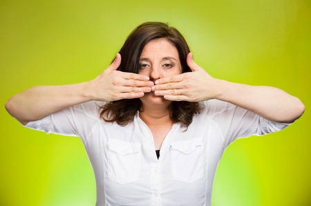 Closeup portrait middle aged woman covering closed mouth. Speak no evil concept, isolated green background. Negative human emotion facial expressions, sign, symbol. Media news coverup, censorshipの写真素材