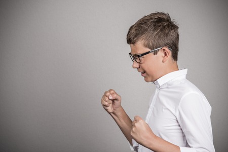 Closeup side view profile portrait angry upset young man teenager boy with glasses fists in air isolated grey wall background.の写真素材