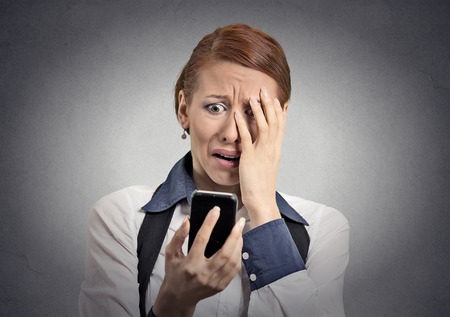 Upset stressed woman holding cellphone disgusted shocked with message she received isolated grey background. の写真素材