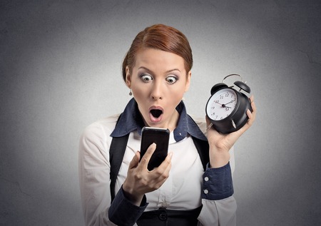 Surprised shocked business woman with alarm clock looking at smart phone with funny  face expression...