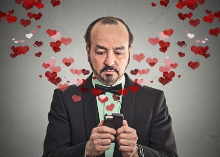 Portrait businessman sending love sms texting with mobile phone isolated grey wall background with red hearts.の写真素材