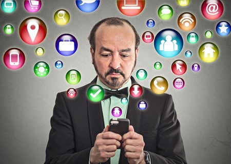 businessman corporate executive using texting on smartphone with social media mobile phone application symbols icons coming flying out of cellphone isolated grey wall background.の写真素材