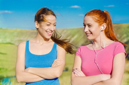 Two attractive happy young women talking and walking together outside on sunny day with blue sky. Positive face expression. Healthy lifestyle, wellbeing, training, life freedom, happiness conceptの写真素材