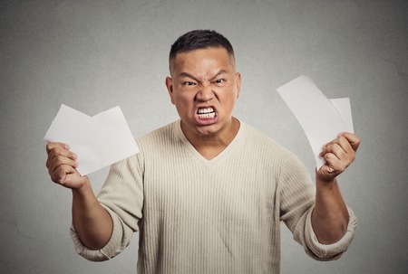 Angry frustrated middle aged man tearing business documents to pieces isolated on grey wall background. Negative human emotions, face expression, feelings, crisisの写真素材