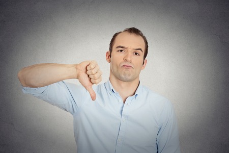 Closeup portrait of angry, unhappy, young handsome man showing thumbs down sign, in disapproval of offer, situation isolated grey wall background. Negative human emotion facial expression feelingsの写真素材