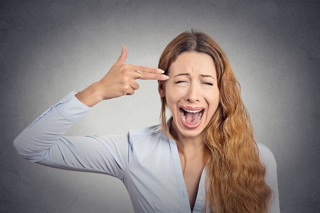Portrait stressed young woman with hand gun gesture screaming isolated on grey wall background. Negative human emotions face expression feelings life perceptionの写真素材