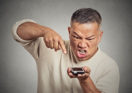 Closeup portrait angry middle aged man, guy, mad worker, pissed off employee while on mobile smart phone isolated grey wall background. Negative emotion facial expressionの写真素材