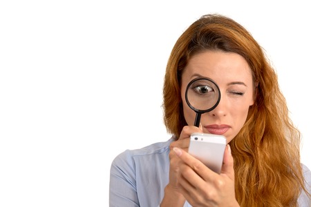 Curious. Business woman looking through magnifying glass at smart phone screen isolated white background. Human face expression. Investigator searching. Security safety concept. Complicated technologyの写真素材