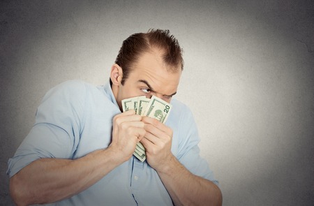 Closeup portrait greedy banker executive CEO boss, corporate employee funny looking man holding dollar banknotes scared to loose money, suspicious isolated grey background. Human face expressionの写真素材