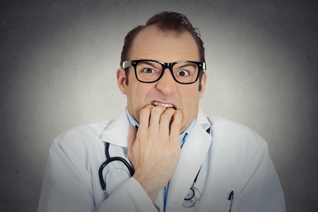 Closeup portrait young insecure, crazy male doctor uncertain psychiatrist with glasses looking funny, scared, craving anxious isolated grey background. Human face expression emotion feeling perceptionの写真素材