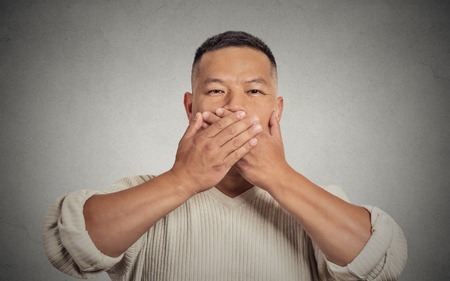 Closeup portrait headshot young man student worker employee covering his mouth with hands. Speak no evil concept isolated grey background. Human face expression feeling sign body language perceptionの写真素材