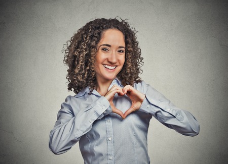 Closeup portrait smiling cheerful happy young woman making heart sign with hands isolated grey wall background. Positive human emotion expression feeling life perception attitude body languageの写真素材