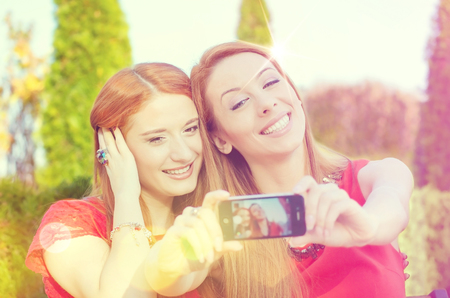 Smiling friends making selfie. Portrait two beautiful carefree young women making selfie and grimacing on a sunny day. Positive face expressions, emotions, feelingsの写真素材