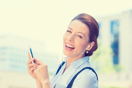 Closeup portrait attractive smiling business woman walking on street listening music on mobile smart...