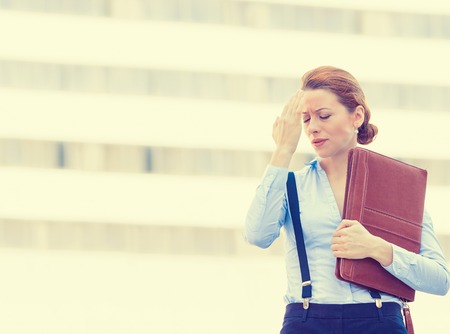 Portrait stressed worried unhappy young woman corporate employee having headache migraine  isolated outdoors on corporate office windows building background. Negative human emotions face expressionの写真素材