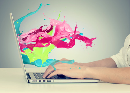 Closeup portrait of business woman's hands on keyboard using laptop with colorful splashes, liquid effect out of monitor screen computer display  isolated on gray background. Creative business concept