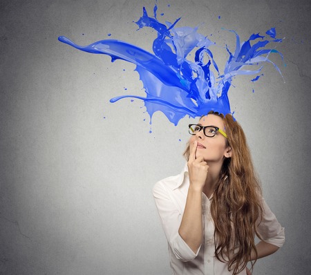 Thoughtful businesswoman looking up with colorful splashes coming out of her head isolated on gray wall background. Face expression perceptionの写真素材