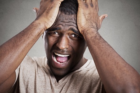 Closeup headshot very sad depressed, stressed disappointed gloomy young man head on hands crying screaming in despair isolated on grey wall background. Human emotion facial expression reactionの写真素材