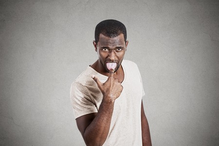 Young angry, unhappy man with finger in mouth something sucks gesture isolated on gray background....