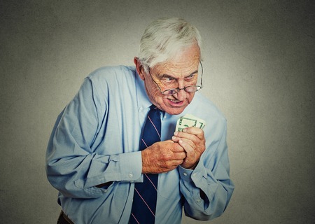 Closeup portrait greedy senior executive, CEO, boss, old corporate employee, mature man, holding dollar banknotes isolated on gray wall background. Negative human emotion facial expressionの写真素材