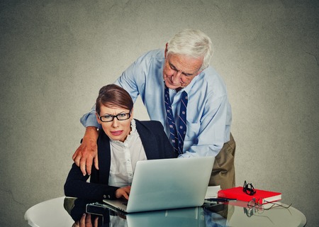 Senior elderly businessman harassing his young colleague at work isolated on gray office wall backgroundの写真素材