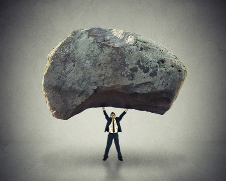 Power of leadership with the ability to inspire as a businessman lifting up a huge boulder removing a large obstacle and leading by example as a business concept of success and determination.の写真素材