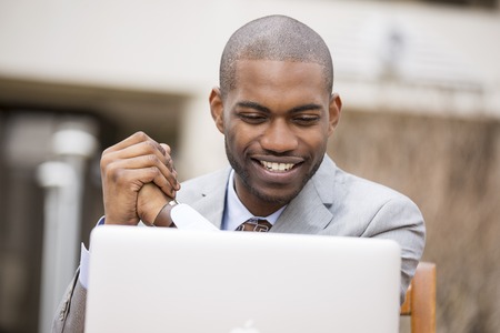 Happy smiling handsome business man with laptop computer sitting outdoorsの写真素材