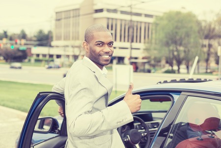 Man driver happy smiling showing thumbs up opening door of a sports blue car isolated outside parking lot city background.の写真素材