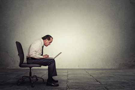 Portrait middle aged man working on laptop sitting on chair in empty office roomの写真素材