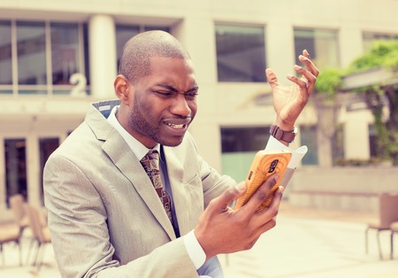 Frustrated handsome young business man in suit receiving bad news message on mobile smart phone standing outdoors outside corporate officeの写真素材